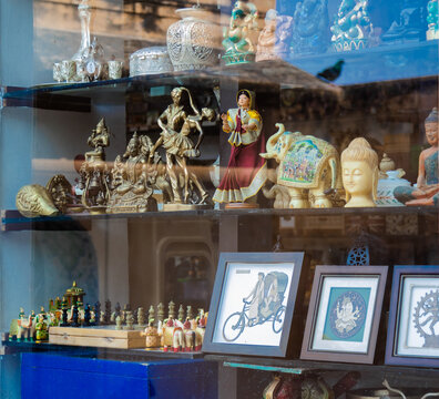 Human figures, toys, photo-frames and Hindu God idols on display with glass pane and a pigeon bird's reflection on it.
