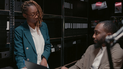 Team of private officers reading witness statements in police archive, trying to catch suspect with...
