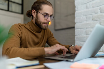 Bearded man freelancer in glasses working at home or in cafe with laptop.