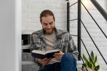 Man reading book while sitting on stairs in his apartment.