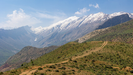 Naklejka premium iran snowy mountains with a hills in the front with a dirt road