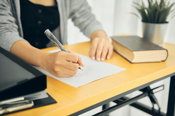 a women holding a pen writing a note on the table . or a student sitting and studying online while in the cafe , home or workplace. 