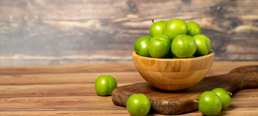 Green plum in bowl. Organic farm products. Fresh plum on wooden background. Copy space. Empty space for text