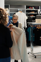 Senior client wanting to buy fashionable clothes, asking store worker for help with casual wear in shopping centre. Elderly woman buying new collection and trendy accessories in modern boutique