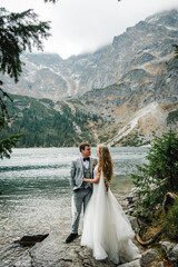 The bride and groom near the lake in the mountains. A couple together against the backdrop of a mountain landscape. Morskie Oko (Sea Eye) Lake. Tatra mountains in Poland.