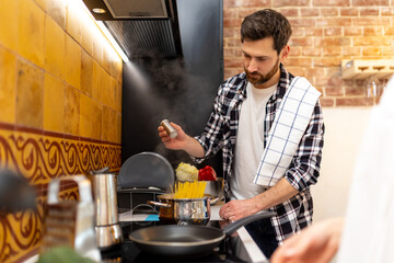 Man cooking healthy meal in kitchenn adding salt to pasta.