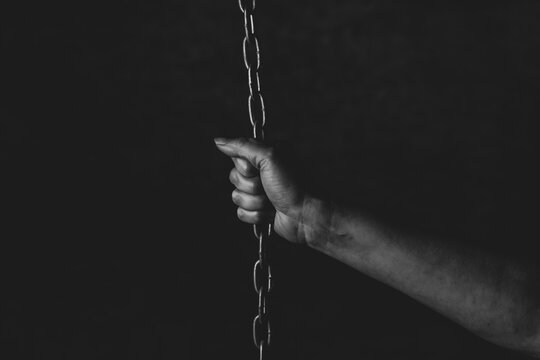 Mano de persona encadenada sobre fondo negro en estudio, sensacion falta de libertad, prision 