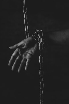 Mano de persona encadenada sobre fondo negro en estudio, sensacion falta de libertad, prision 