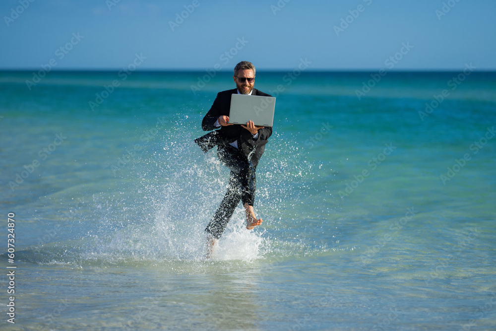 Wall mural Excited summer business travel. Freelance work, online working. Summer businessman in suit run in sea water. Freelance travel. Funny freelancer in suit jump and run in the sea. Freelance and holidays.