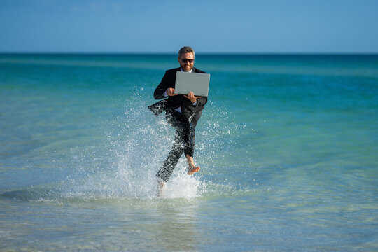 Excited summer business travel. Freelance work, online working. Summer businessman in suit run in sea water. Freelance travel. Funny freelancer in suit jump and run in the sea. Freelance and holidays.