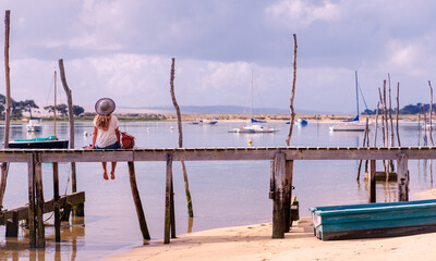 Woman sitting on wooden pier looking at harbor,  Arcachon Basin,  Landes in France