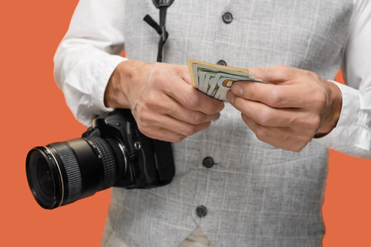 Closeup photo of male professional photographer with camera holding dollars cash, The currency serves as a tangible symbol of the photographer's successful endeavors