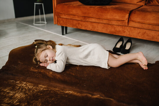 Baby sleeping in living room. Little girl is lying down on a carpet on floor, she was playing and putting on her mother's shoes and tired. Funny tired child falling asleep crawling on floor at home.