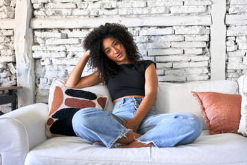 Afro-haired woman relaxes on sofa, basking in soft morning light at home.