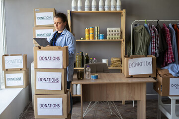 Woman check-out donation food according to list on clipboard working at distribution or refugee...