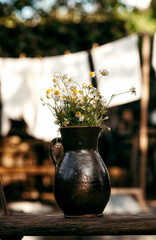 An earthenware jug with daisies stands against the background of green trees