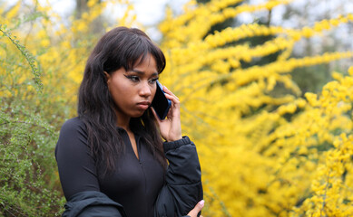 Black woman talking on the phone near the flowers in the park.