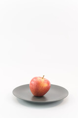 immagine primo piano di mela matura rosso gialla su piatto in ceramica grigio, sfondo superficcie bianca