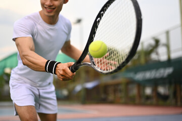 Shot of male athlete hitting ball with racket on outdoor court. Fitness, sport, exercise concept