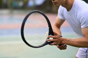 Male tennis player focused in ready position to receive a serve, practicing for competition on a court