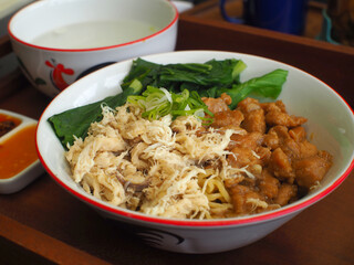 Asian chicken noodles complete set with soup and chili oil on a wooden tray.