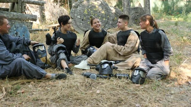 Happy group of paintball players with guns after match on paintball playing field 