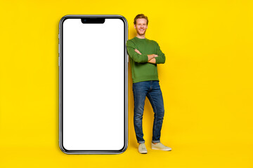 Full length photo of charming handsome guy dressed sweater arms folded modern device empty space isolated yellow color background