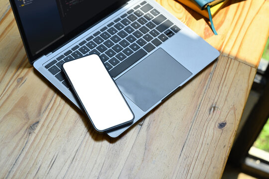 Smartphone with white blank screen and laptop computer on wooden office desk