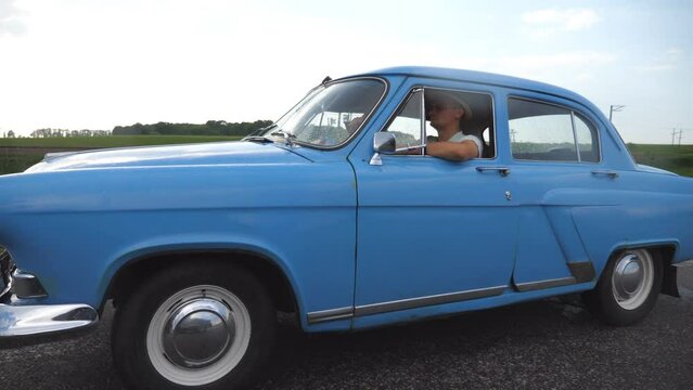 Classic old car traveling on highway on summer day. Young couple driving on country road in vintage automobile. Trip at the retro auto. Concept of summer vacation or holiday. Slow motion Close up