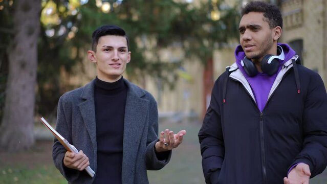 Caucasian and African American groupmates walking discussing studies in slow motion outdoors. Front view portrait of intelligent young students strolling at campus talking