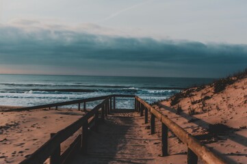 Obraz premium Beautiful view of the pathway in sand heading to the ocean with cloudy sky.