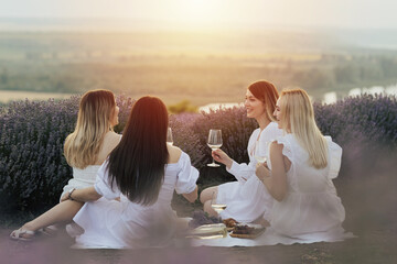 Lovely ladies drinking wine in lavender violet field at sunset. Summer happy mood. Girlfriends relaxing on summer sunset with river on the background.	