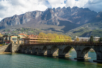 Buildings of the city of Lecco on the banks of the river Adda. Bridges and an island with mountains in the background - obrazy, fototapety, plakaty