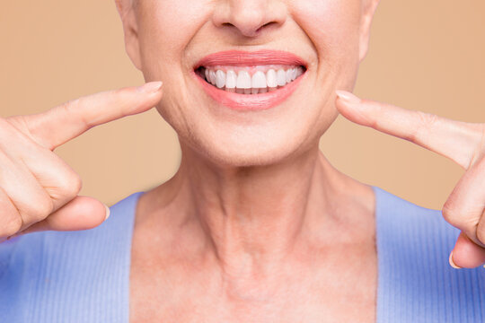 Concept of having strong healthy straight white perfect teeth at old age. Cropped portrait of beaming smile female pensioner pointing on her teeth, isolated over violet background