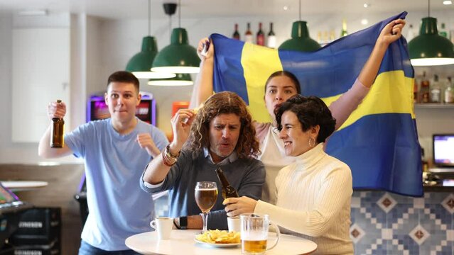 Joyful friends with the flag of Sweden celebrating the victory of their favorite team in a beer bar. High quality 4k footage