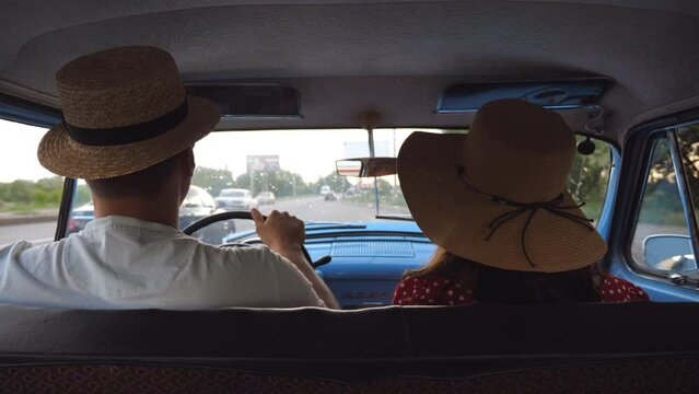 Young couple in hats riding at vintage car during road trip. Unrecognizable man and woman sitting at the front seat of old retro car. Travel concept. Slow motion Rear back view Close up