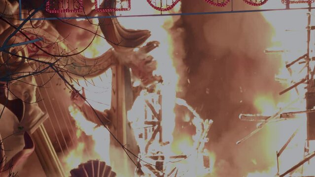The celebration of Fallas on the streets of Valencia, Spain, as a large ninot figure resembling a girl with a harp burns against the backdrop of the night sky