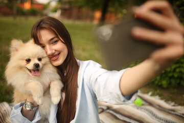 Caucasian girl student female pet owner taking selfie photo with dog, image on smart phone, having video call conversation with dog online in park