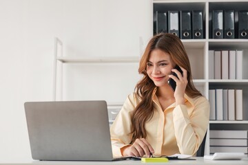 Portrait of financial business woman sitting at desk and working on laptop while making talk on the phone