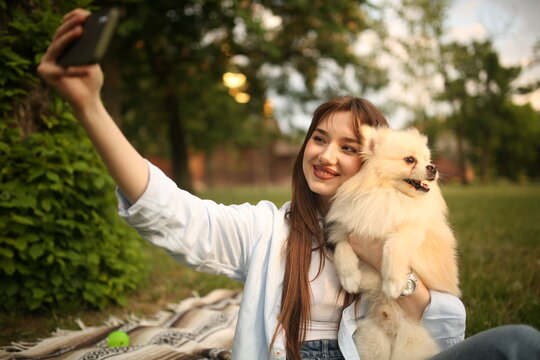 Caucasian girl student female pet owner taking selfie photo with dog, image on smart phone, having video call conversation with dog online in park