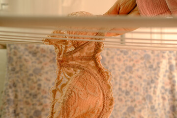 female hands of middle-aged woman close-up hang wet washed linen, bra on wire dryer, gentle hand...