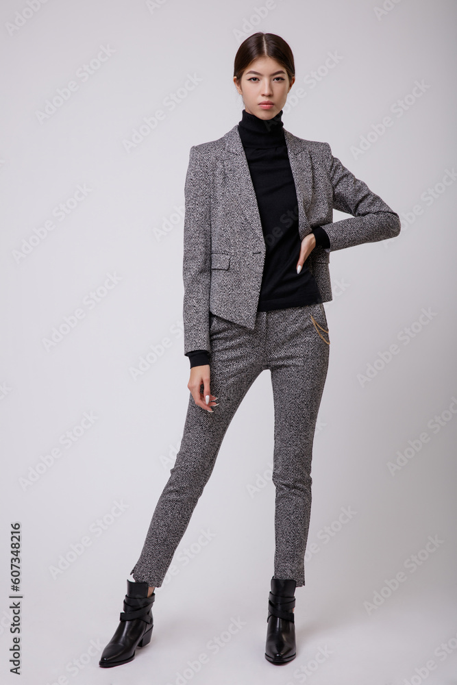 Wall mural Fashion photo of a beautiful elegant young asian woman in a pretty gray suit, pants, trousers, jacket, blazer, black top posing over white, soft gray background. Studio Shot, portrait. Slim figure