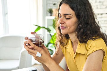 A young Caucasian woman, seated on the sofa, savoring a cup of tea in the morning light, enjoying a serene moment.