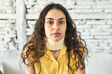 A resilient young Caucasian woman, sitting on the sofa with a neck brace, embracing healing and...