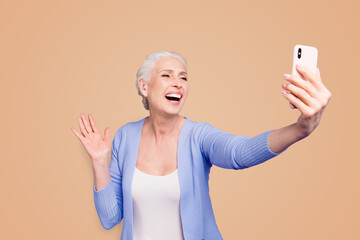 Grey haired old happy excited funny funky woman wearing casual, taking self picture, waving to cam, opened mouth. Isolated over violet purple background