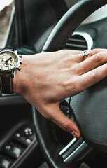 A man holds the steering wheel of a luxury car. Watch and a ring on his hand - 607351229