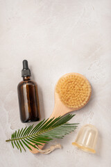 Bottles of dark amber glass with essential oil, cream, massage brush and tropical leaves