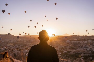Rear view of a male enjoying the sunrise and hot air balloons rising up in Cappadocia, Turkey