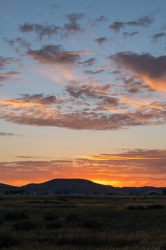 Beautiful shot of an orange sunset over mountains and fields © Rizzvisuals/Wirestock Creators