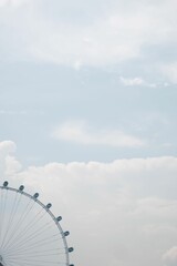 Vertical shot of a Ferris wheel against a blue cloudy sky